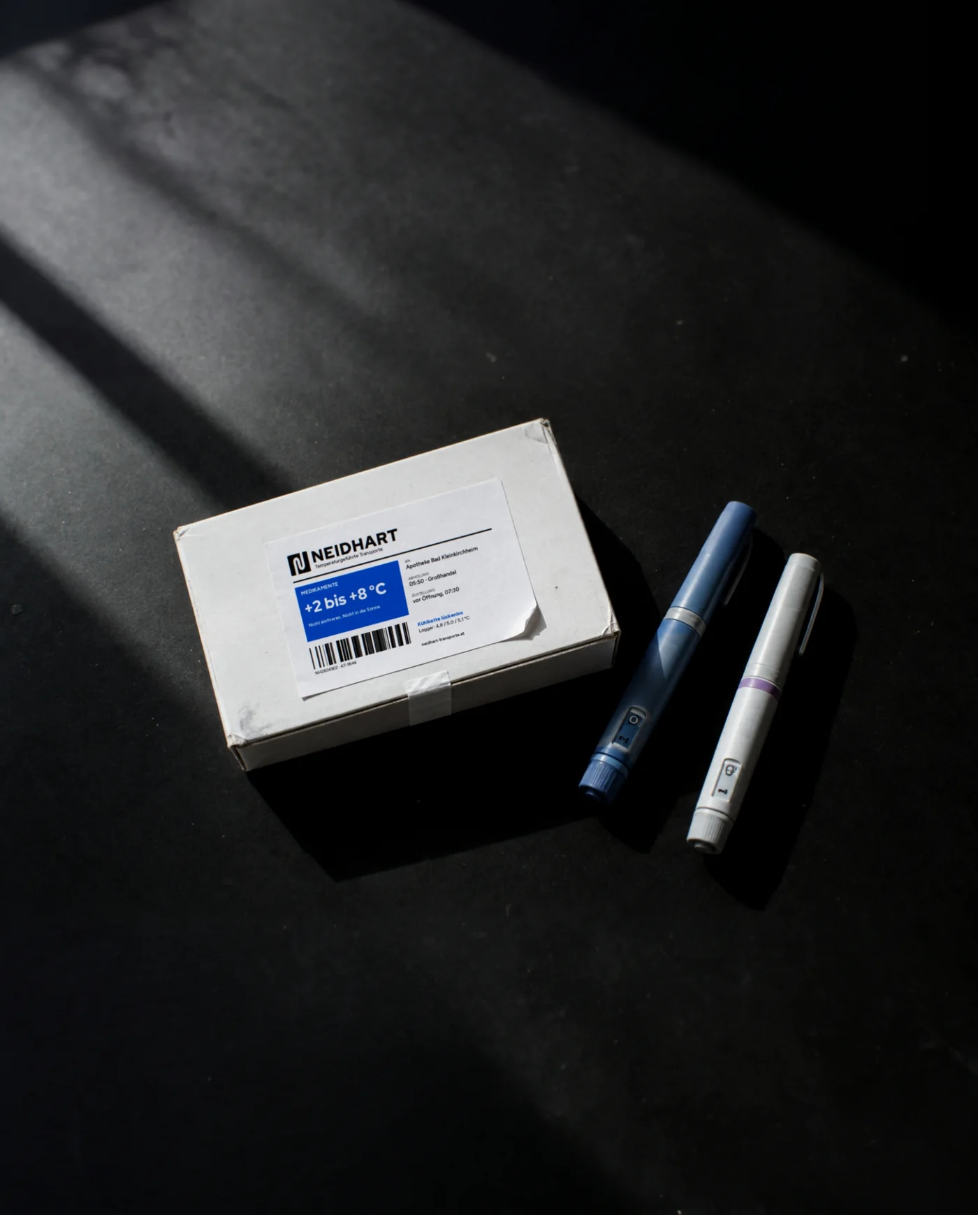 Medikamentenpackung mit Neidhart Etikett und zwei Insulin-Pens auf schwarzem Grund